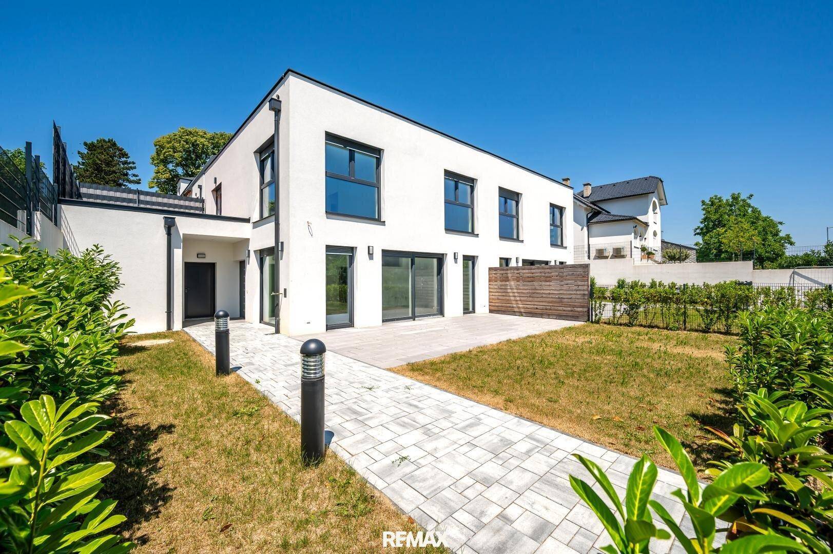 Moderne weiße Fassade eines Neubaus mit großen Fenstern und angrenzender Terrasse unter klarem Himmel.