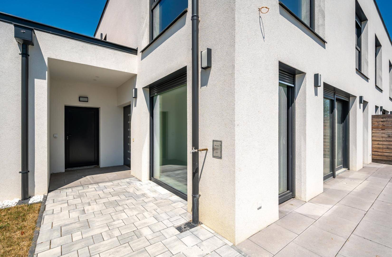 Eingangsbereich des modernen Hauses mit überdachtem Zugang und großen Fenstern mit Rollläden.