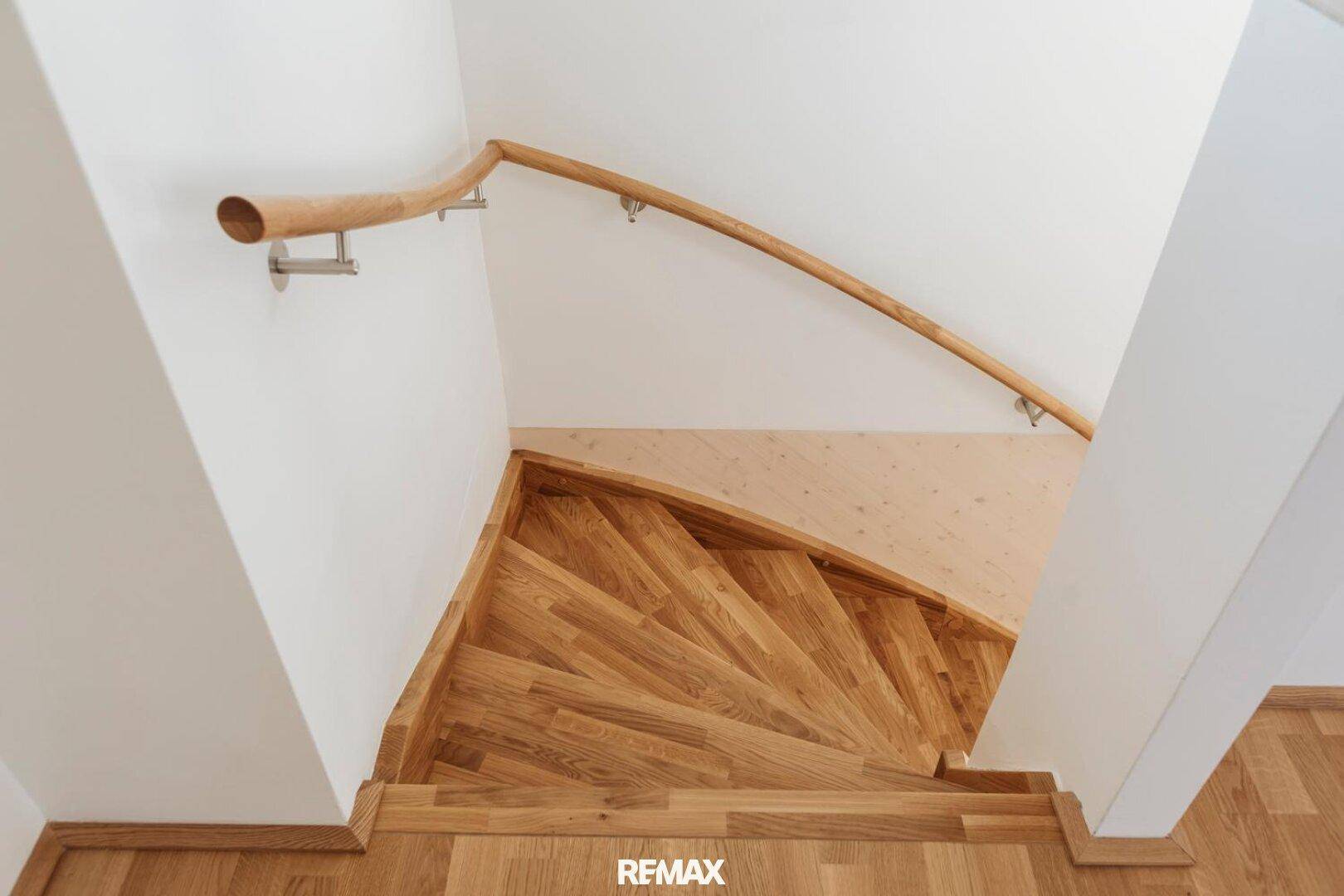 Elegante Holztreppe mit geschwungenem Handlauf in einem hellen Treppenhaus.