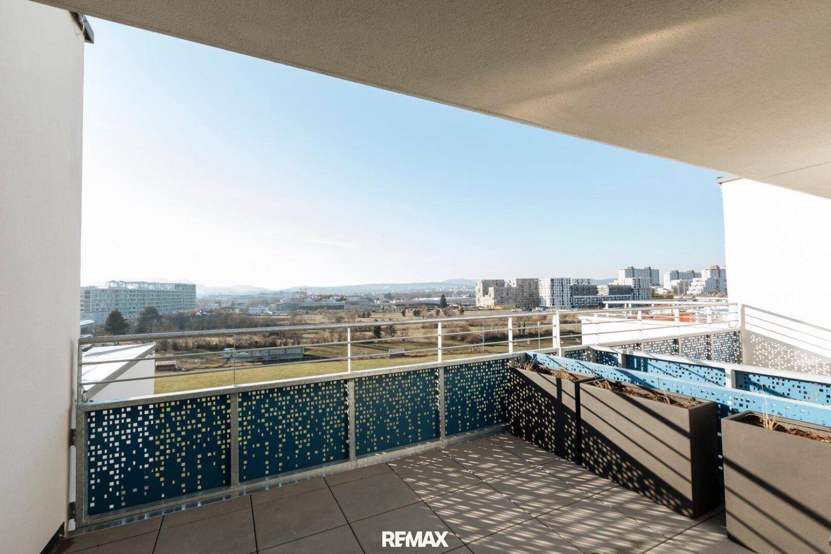 Geräumige Terrasse mit weitem Stadtblick und modernen blauen Brüstungselementen.