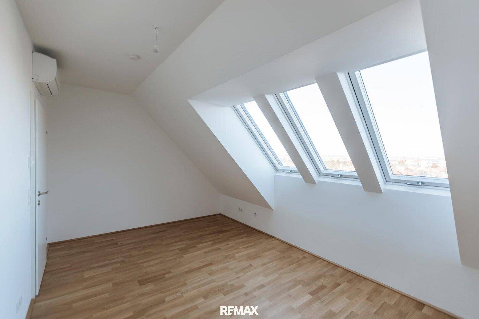 Heller Raum im Dachgeschoss mit Holzboden, Dachschräge und schrägen Dachfenstern.
