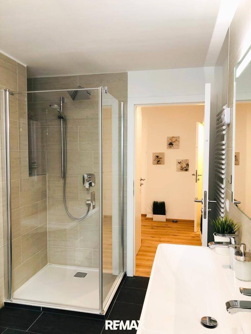 Modernes Badezimmer mit großer Duschkabine, Waschbecken und beheiztem Handtuchhalter.