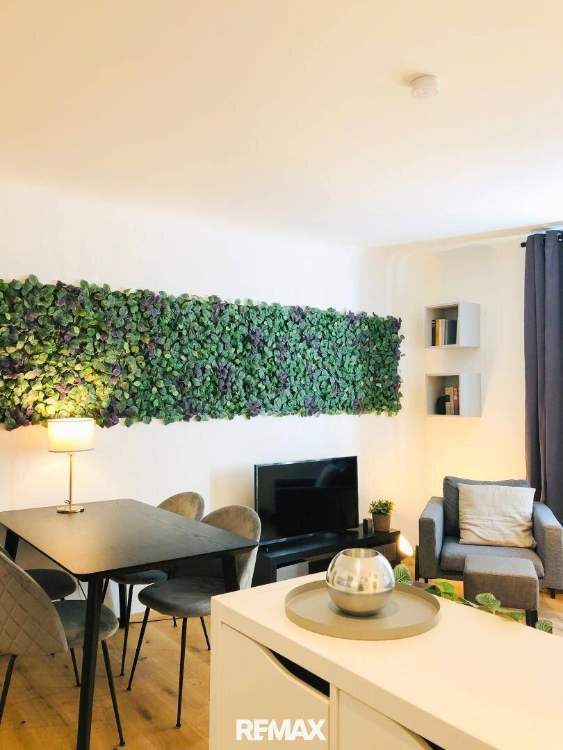 Moderner Wohn-Essbereich mit Holzboden, Esstisch und dekorativer grüner Pflanzenwand.
