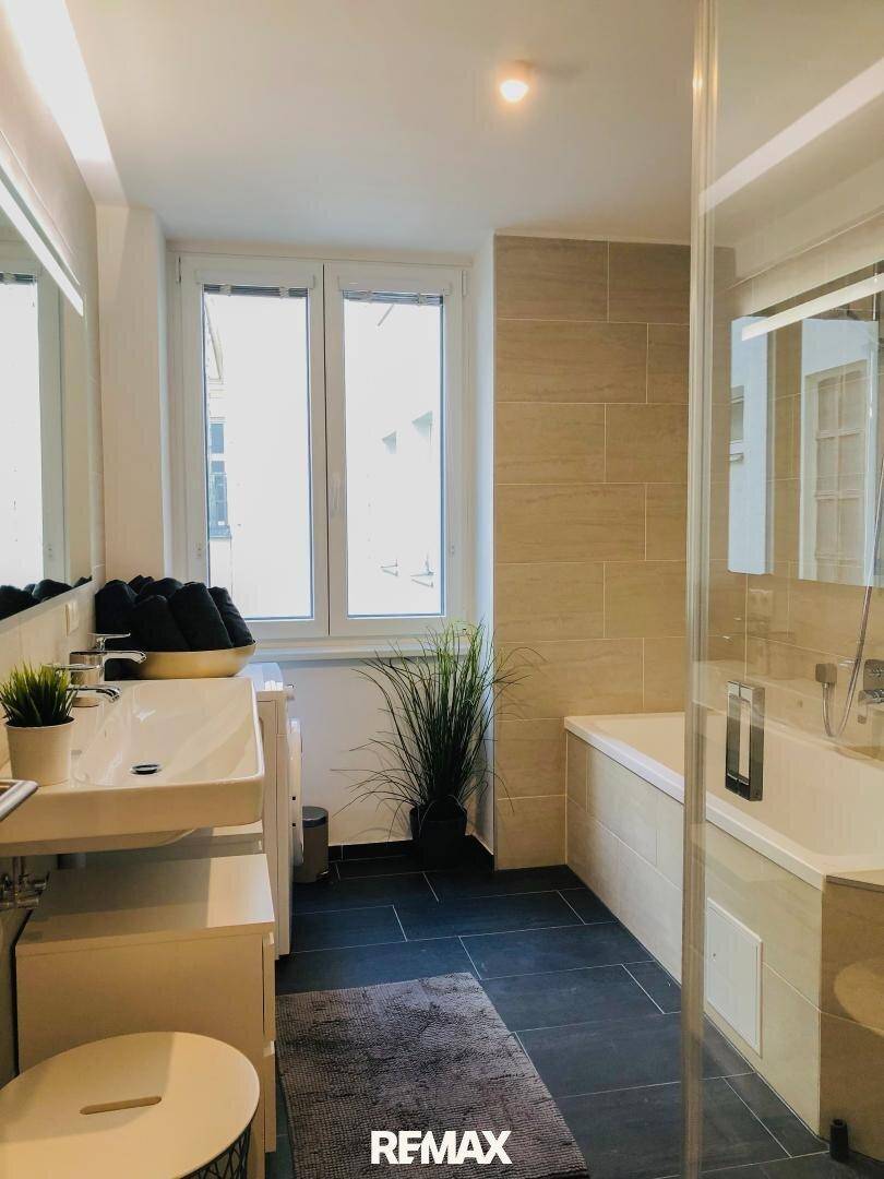 Helles Badezimmer mit Badewanne, Dusche, modernem Waschbecken und Fenster für Tageslicht.