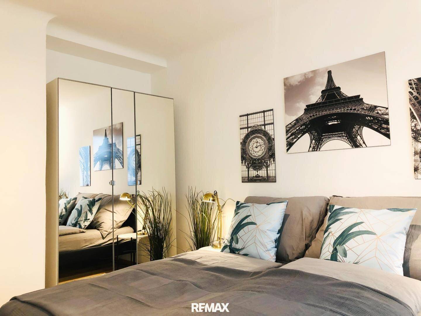 Schlafzimmer mit großem Bett, Spiegelschrank und Pariser Motiven als Wanddekoration.