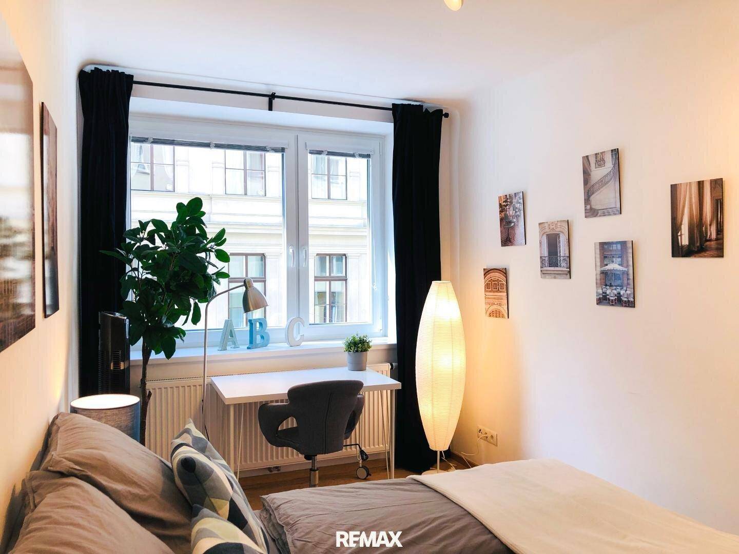 Gemütliches Schlafzimmer mit Schreibtisch, großem Fenster und dekorativen Bildern an der Wand.