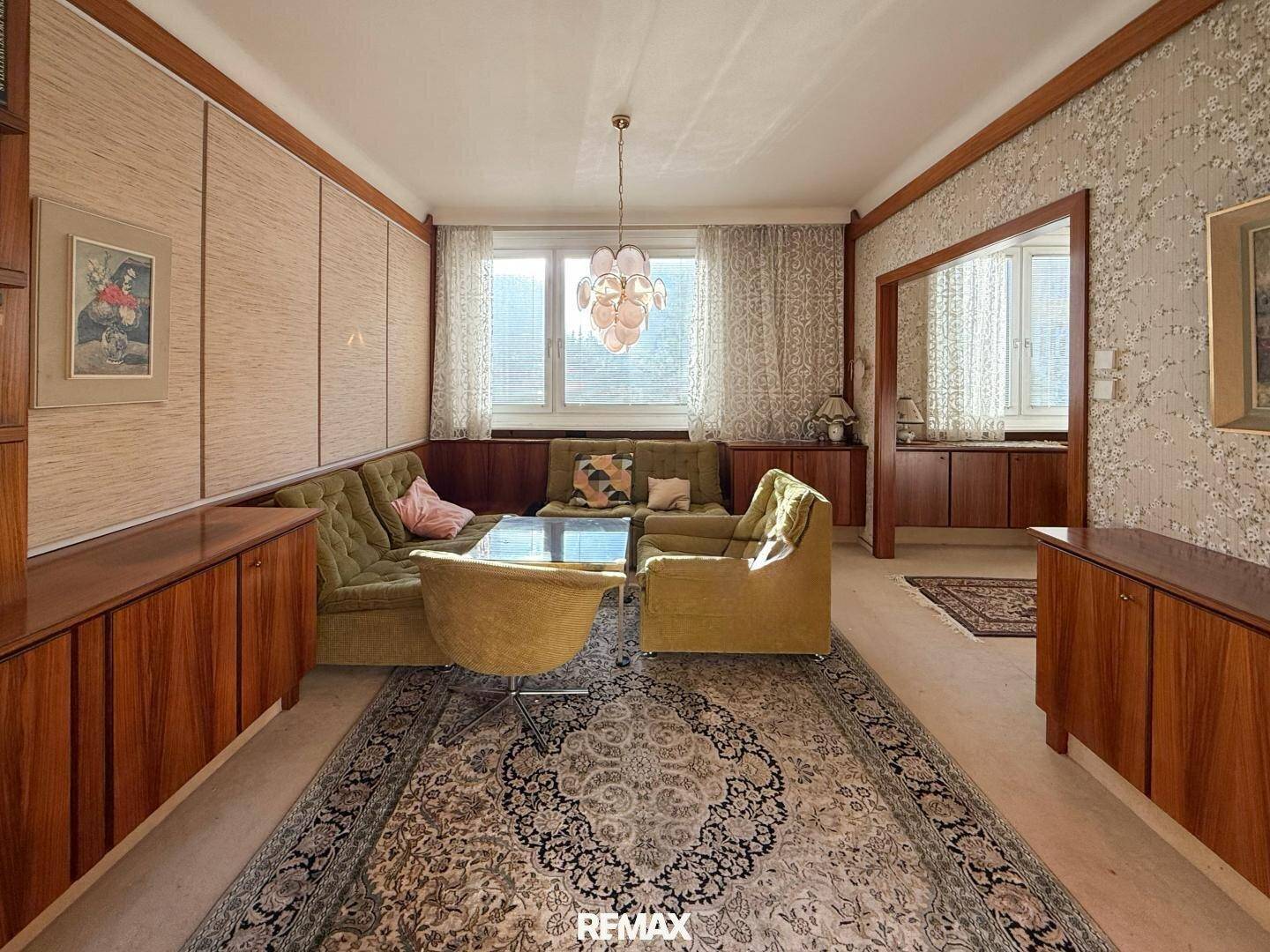 Geräumiges Wohnzimmer im Vintage-Stil mit grünen Sitzmöbeln und dunklen Holzvertäfelungen.