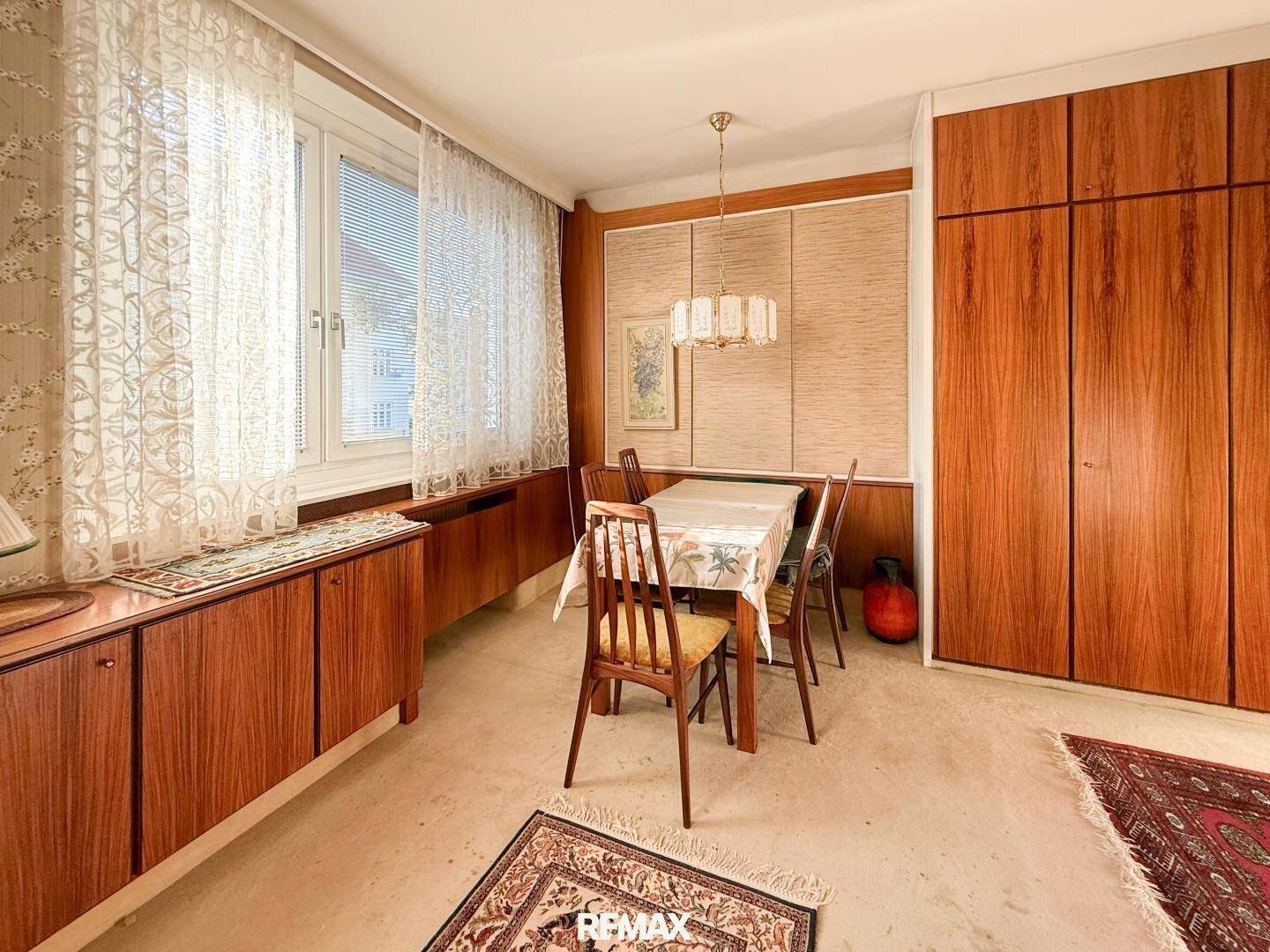 Esszimmer mit Holztisch und Stühlen, Fenster mit Vorhängen und Holzvertäfelungen.