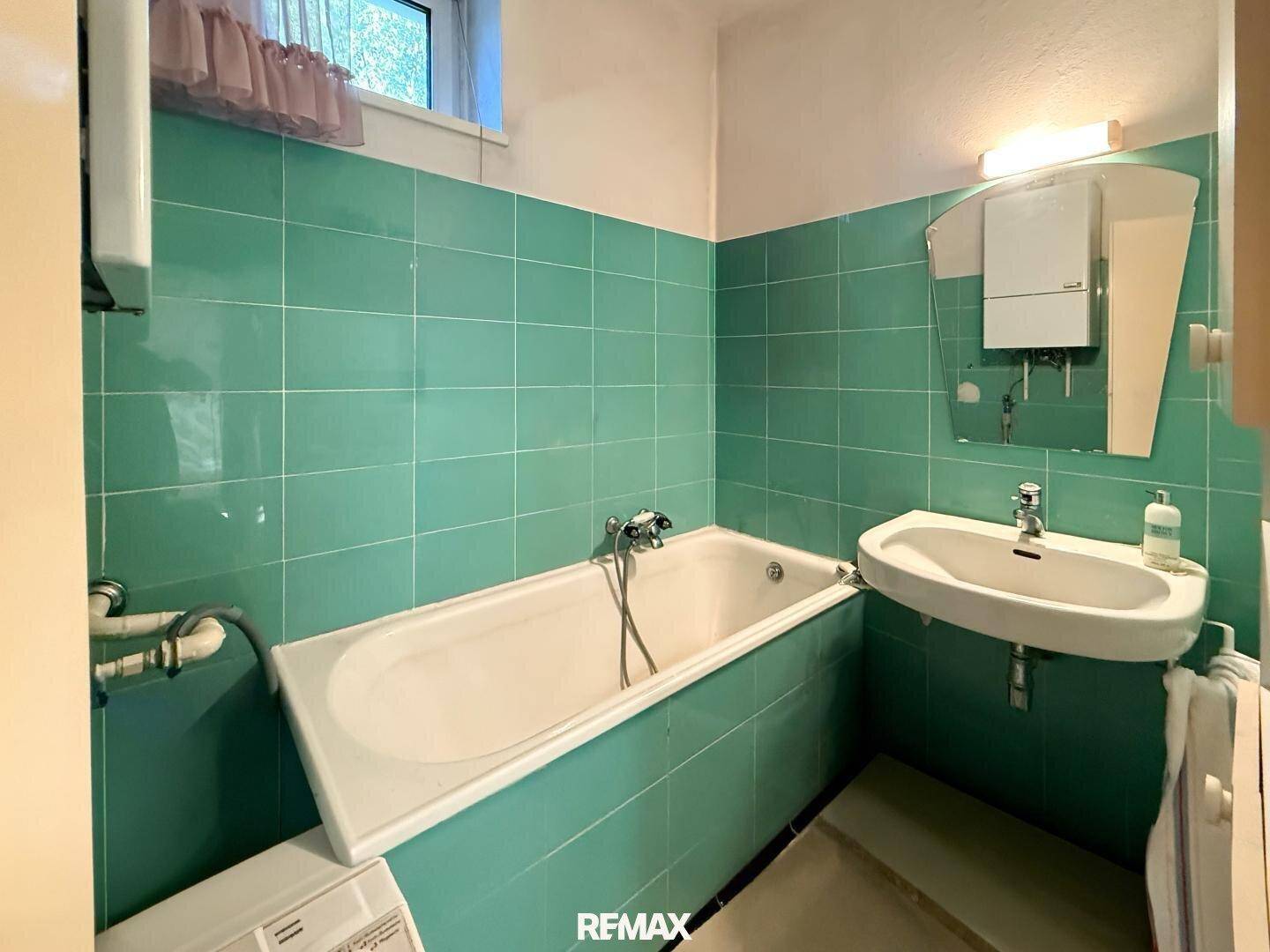 Badezimmer mit grünen Fliesen, Badewanne und Waschbecken im 80er-Jahre-Stil.