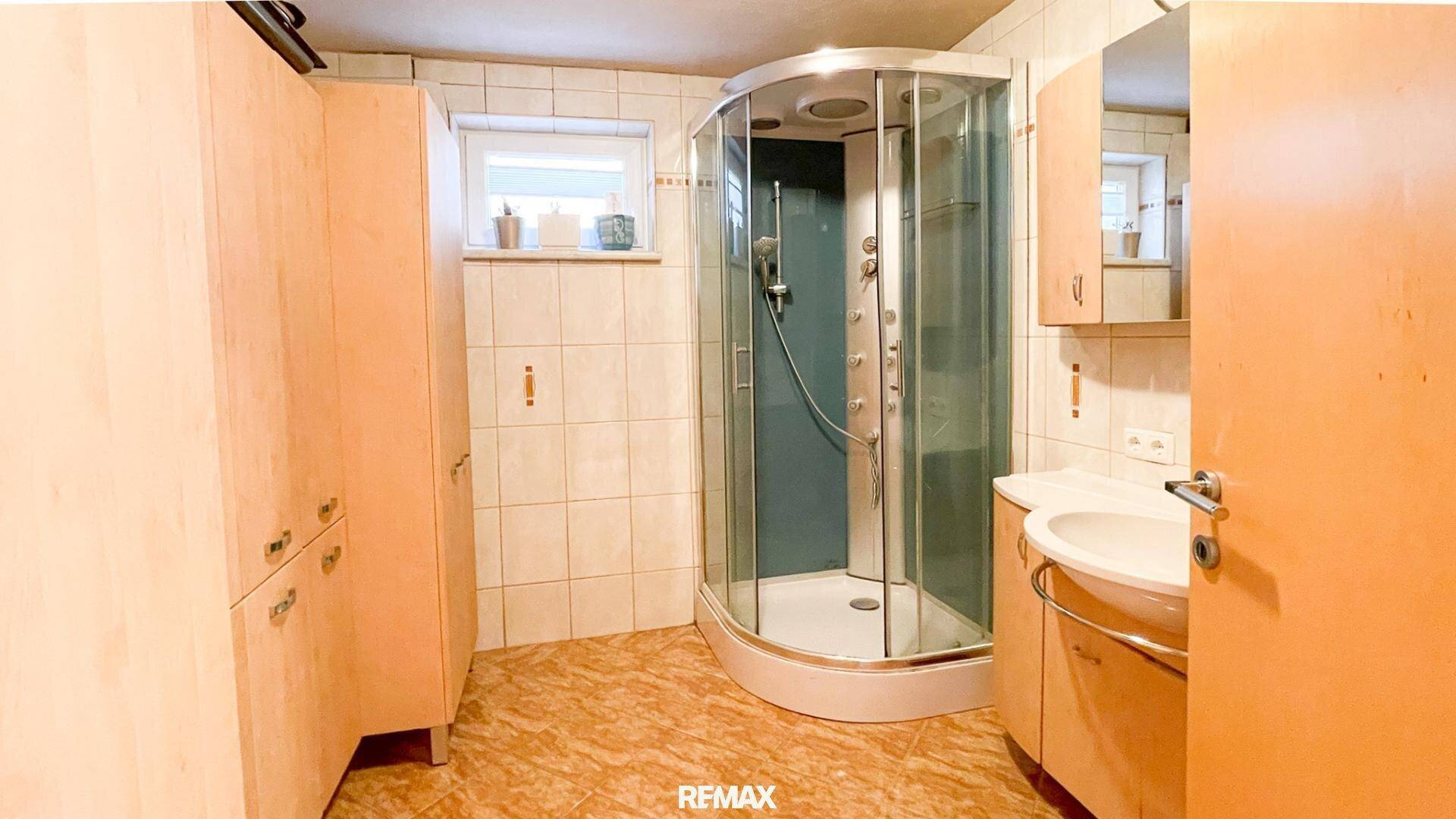 Badezimmer mit Duschkabine, Waschbecken und Holzschränken, funktional eingerichtet.