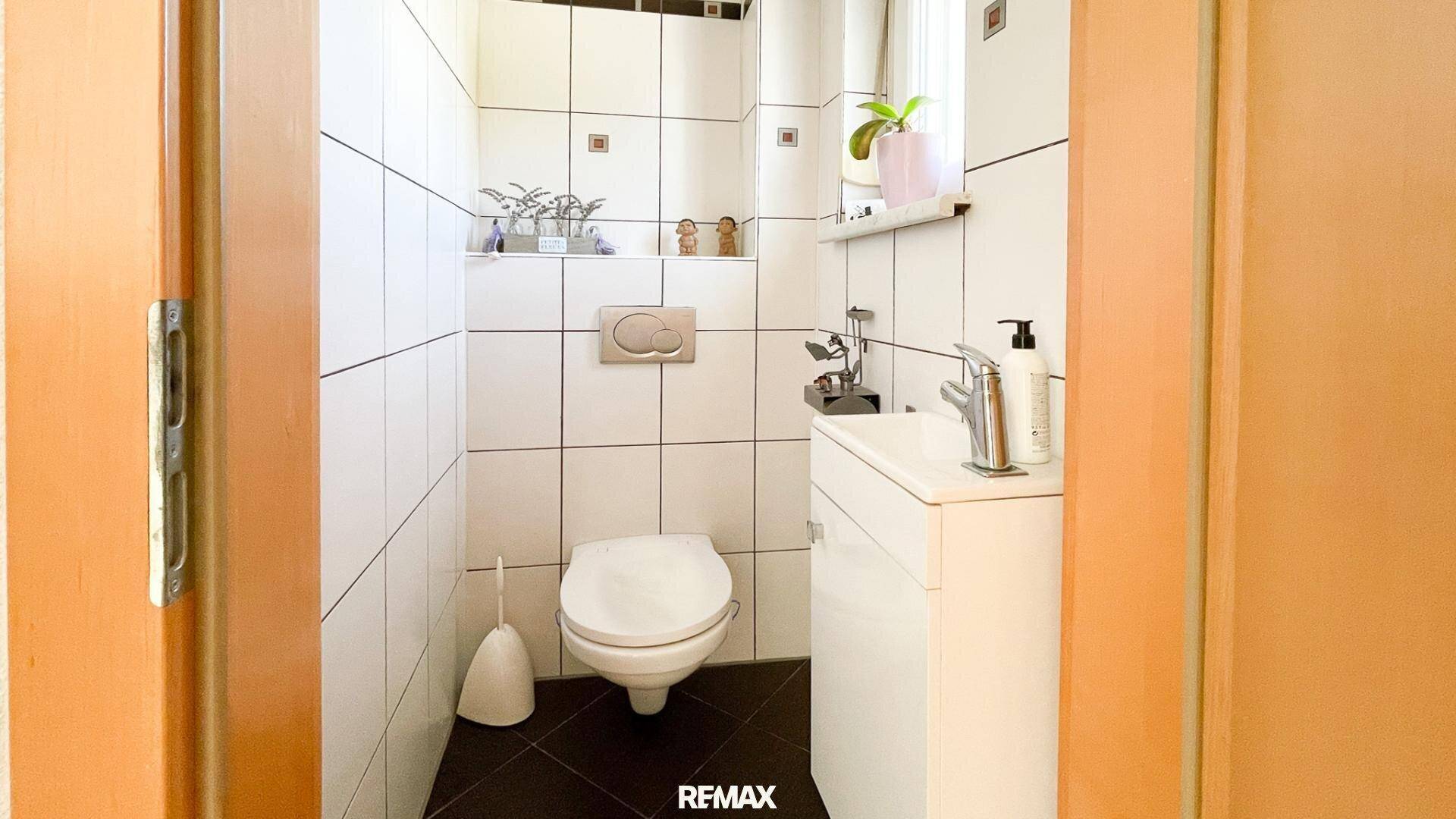 Kleines Gäste-WC mit weißen Fliesen, wandhängendem WC und Waschbecken mit Unterschrank.