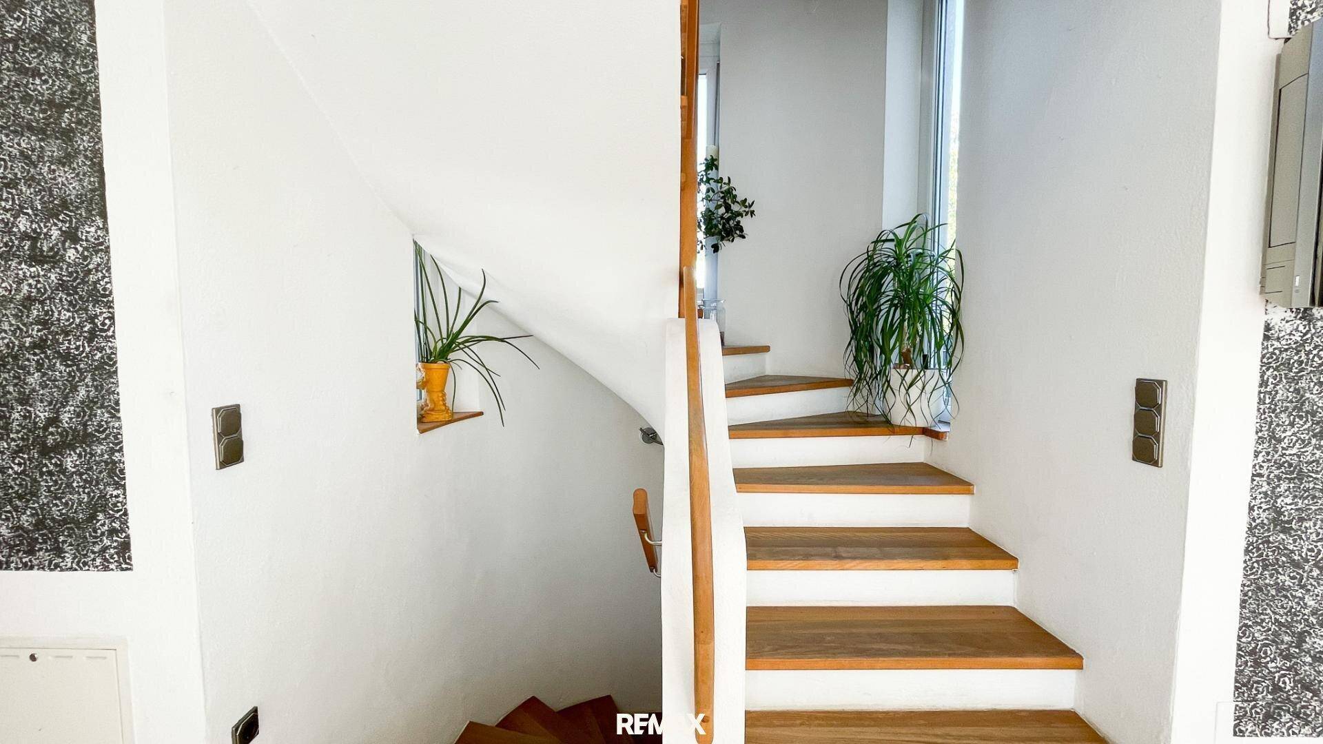 Holztreppe mit weißem Geländer und natürlichem Lichteinfall, die die Stockwerke verbindet.