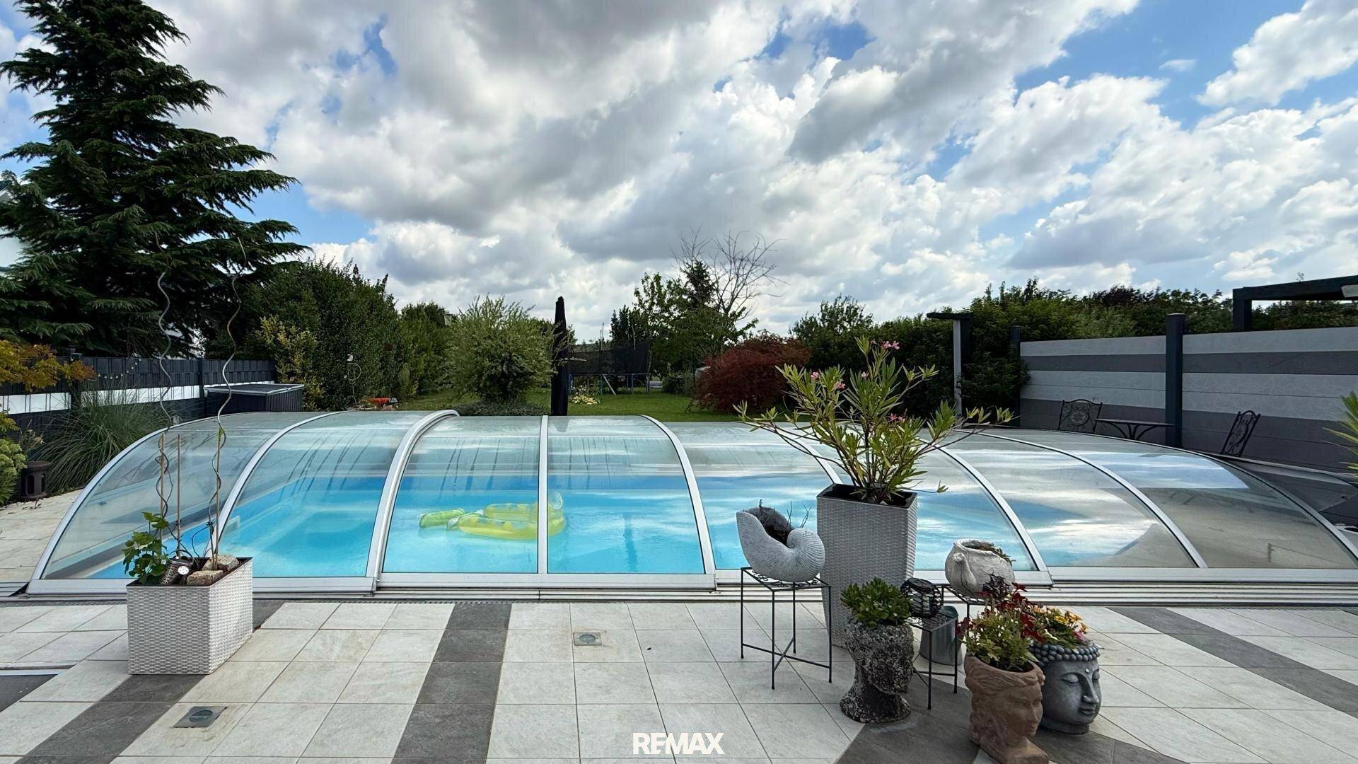 Überdachter Poolbereich mit gepflasterter Terrasse und dekorativen Pflanzen im Garten.