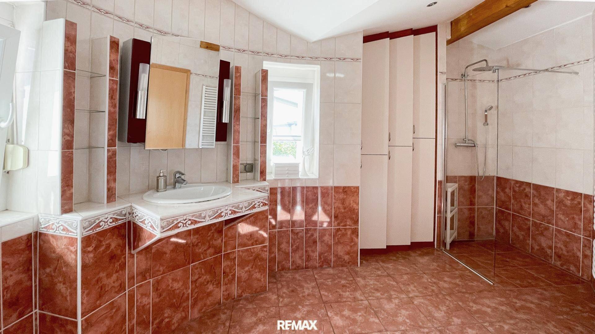 Badezimmer mit roten und weißen Fliesen, Duschbereich und Waschbecken mit Spiegelschrank.