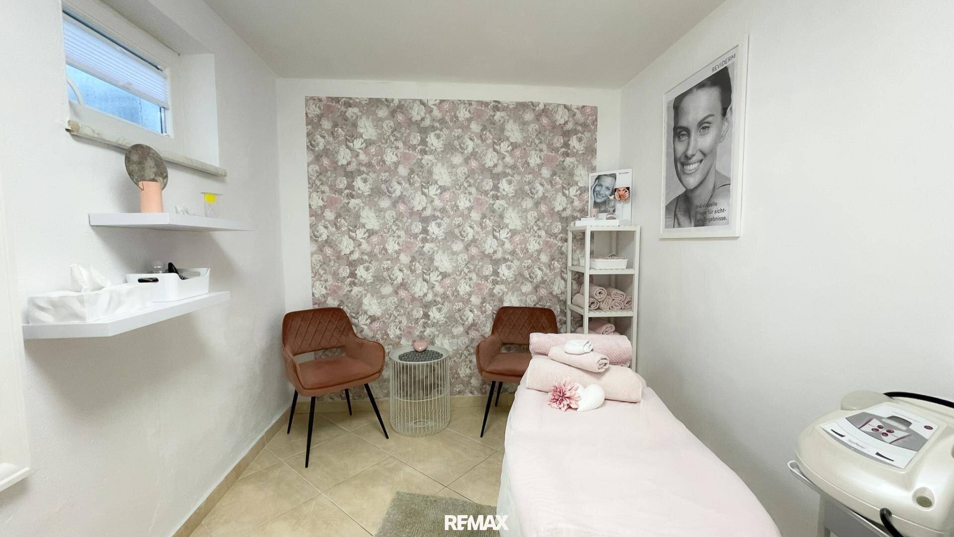 Heller Raum mit floraler Akzentwand, Fliesenboden und Liege, möglicherweise ein Behandlungszimmer.