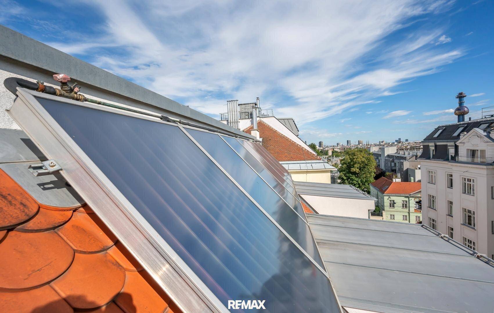 Solarpaneele auf einem Ziegeldach mit Blick auf die umliegende Stadtlandschaft unter blauem Himmel.