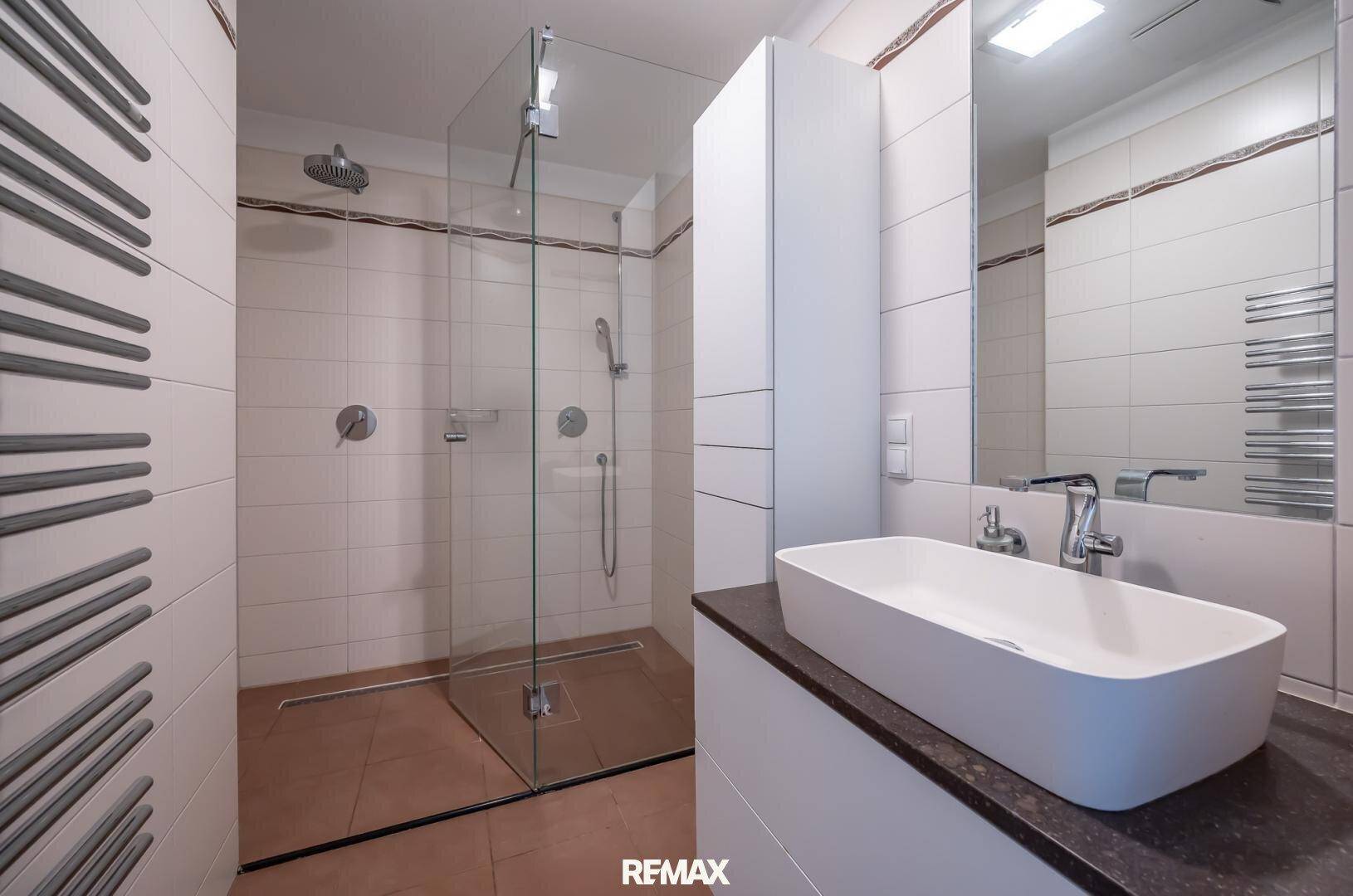 Modernes Badezimmer mit ebenerdiger Dusche, elegantem Waschbecken und beheiztem Handtuchhalter.