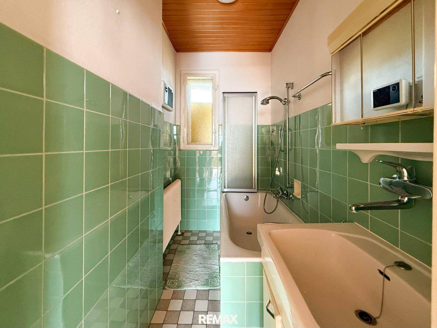 Badezimmer im Stil der 80er Jahre mit grünen Fliesen, Badewanne und Waschbecken.
