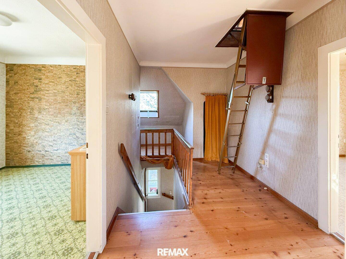 Geräumiger Flur mit Holzfußboden, Dachfenster und Zugang zum Dachboden über eine Leiter.