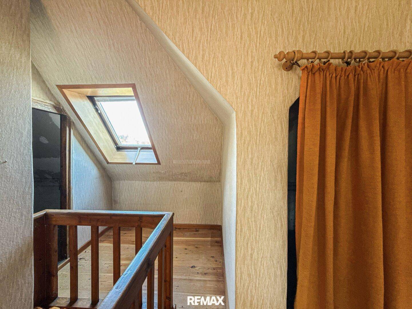 Dachgeschossflur mit Holzfußboden, Dachfenster und Holzgeländer, das den Raum strukturiert.