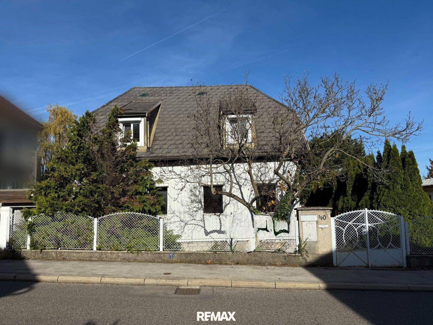 Älteres Einfamilienhaus mit Mansarddach und Garten, von der Straße aus gesehen.