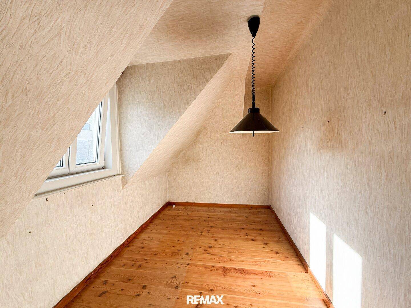 Helles Dachzimmer mit Holzfußboden und schrägen Wänden, ideal als Schlafzimmer oder Büro.