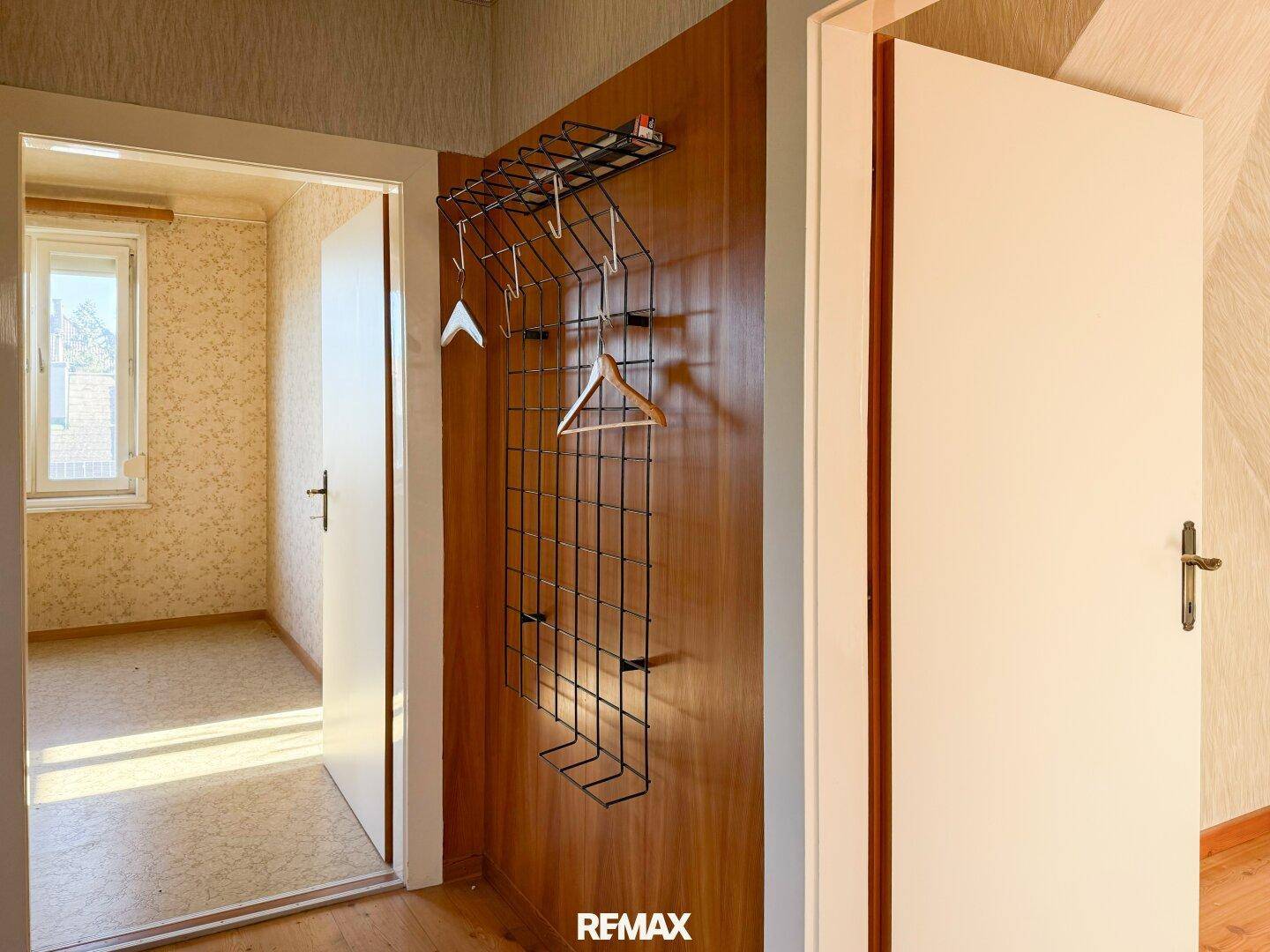 Flur mit Garderobe und Zugang zu einem weiteren Zimmer mit Korkboden und Fenster.