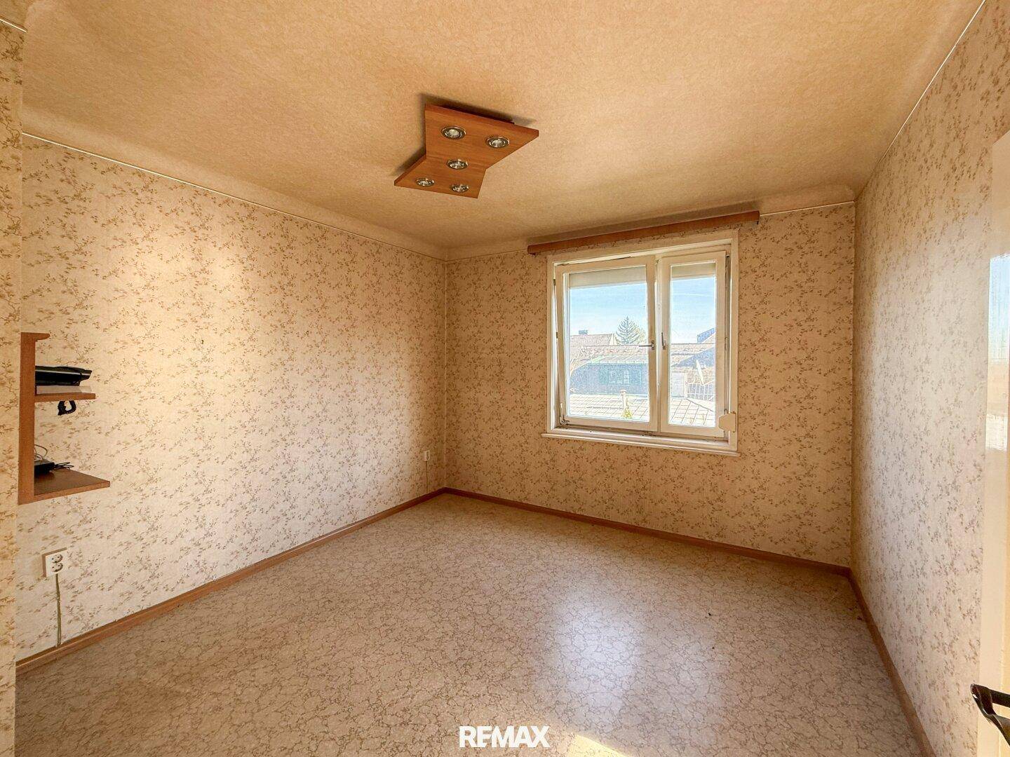 Zimmer mit Korkboden und Fenster, das einen Blick nach draußen ermöglicht und den Raum belichtet.