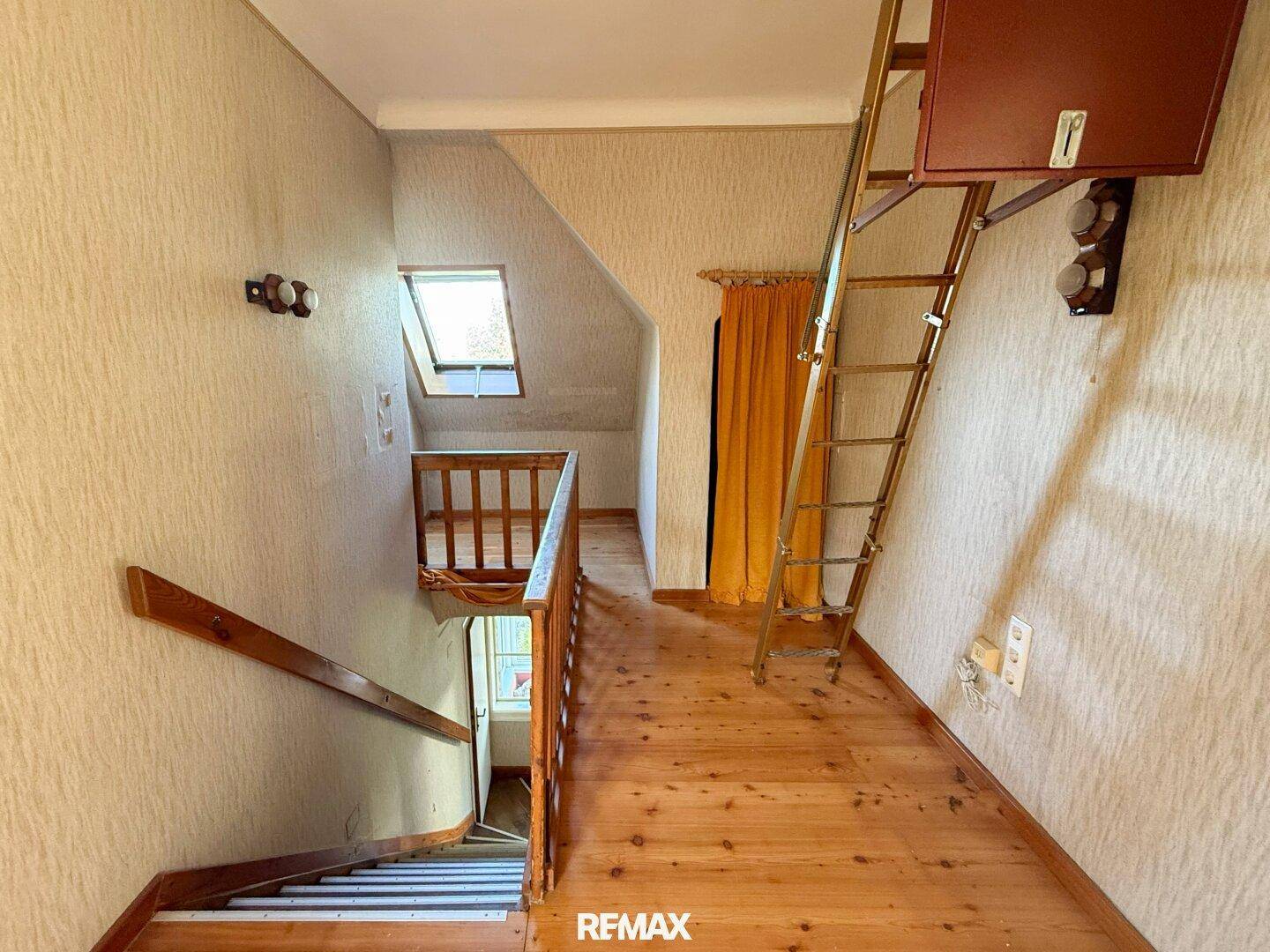 Flur mit Holzfußboden, Dachfenster und einer Leiter zum Dachboden, der zusätzlichen Stauraum bietet.