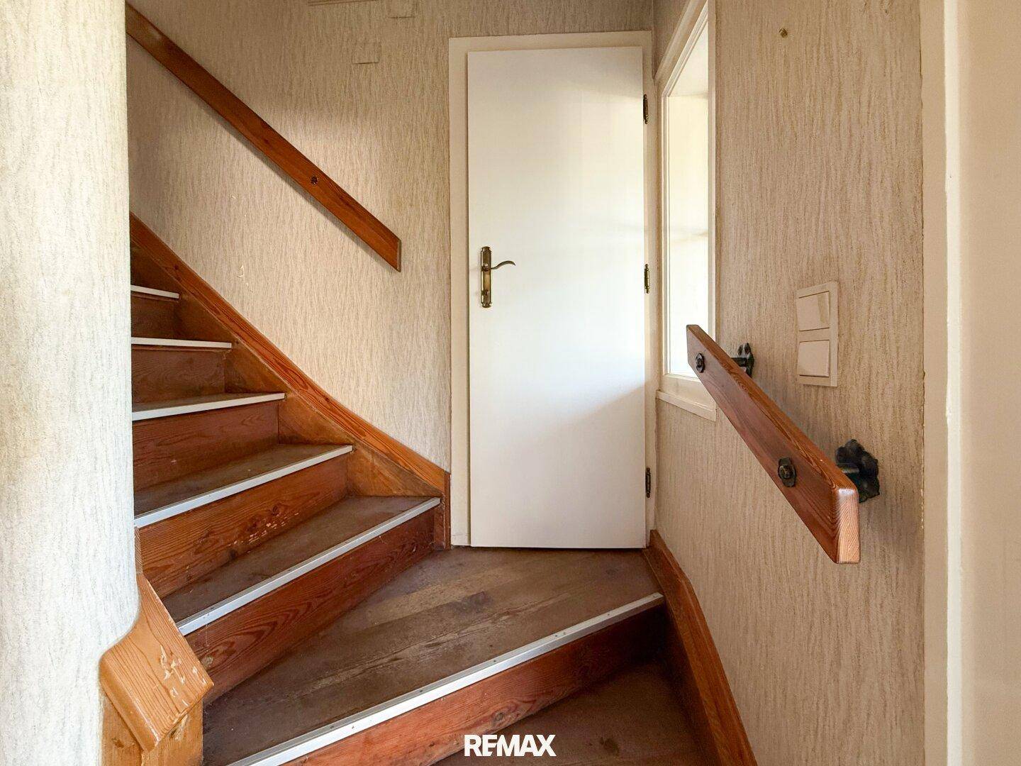 Holztreppe mit Handlauf in einem Flur mit strukturierten Tapeten, die nach oben führt.