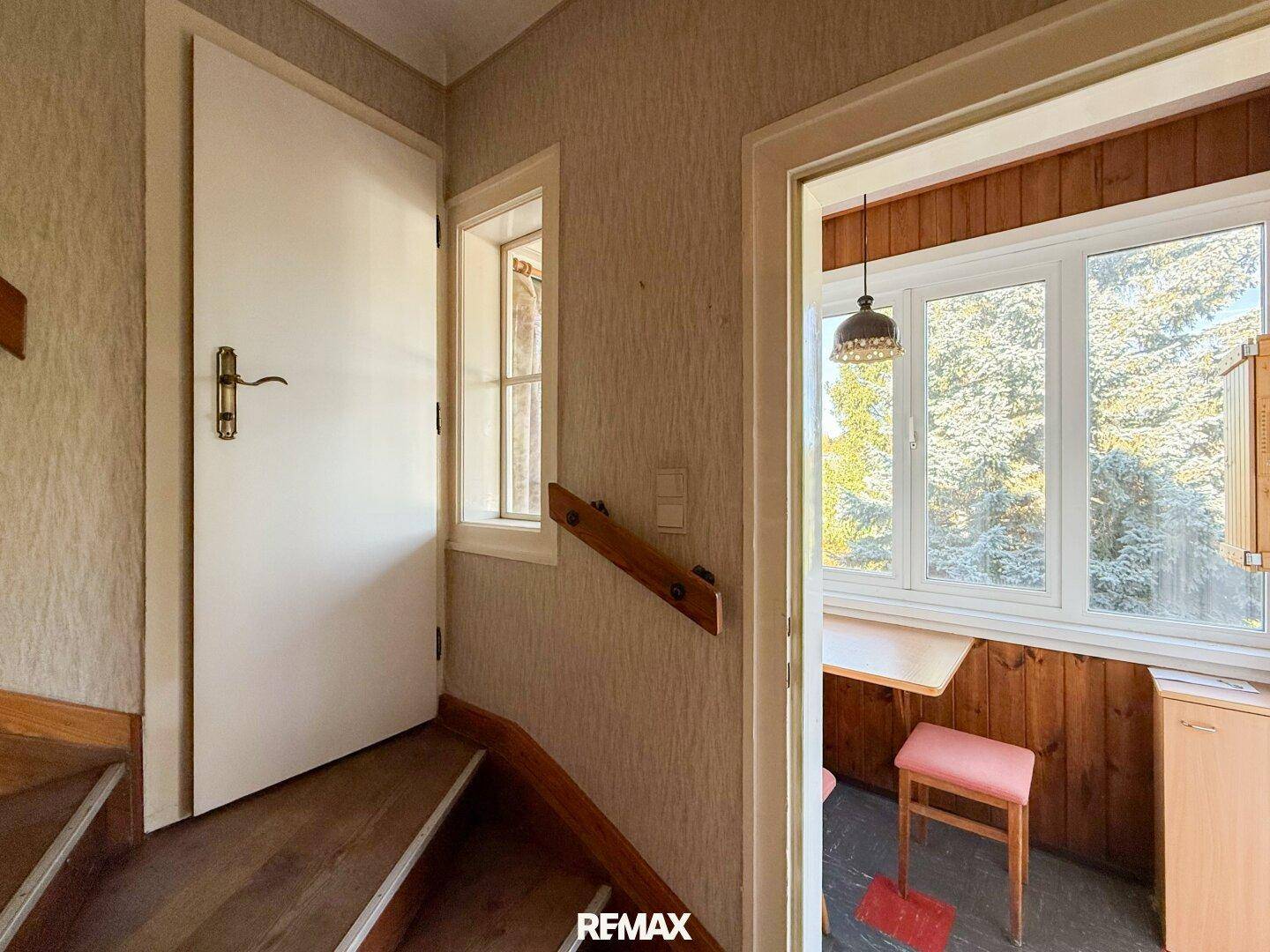 Treppenaufgang mit Holztüren und einem Fenster, das Tageslicht hereinlässt.