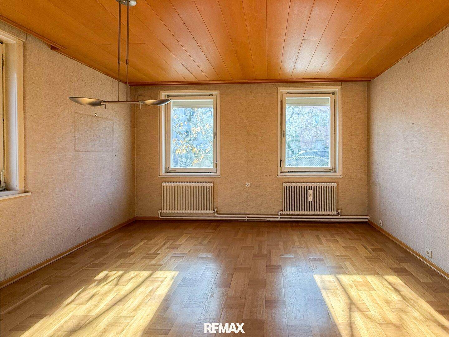 Helles Zimmer mit Parkettboden, Holzdecke und zwei Fenstern.
