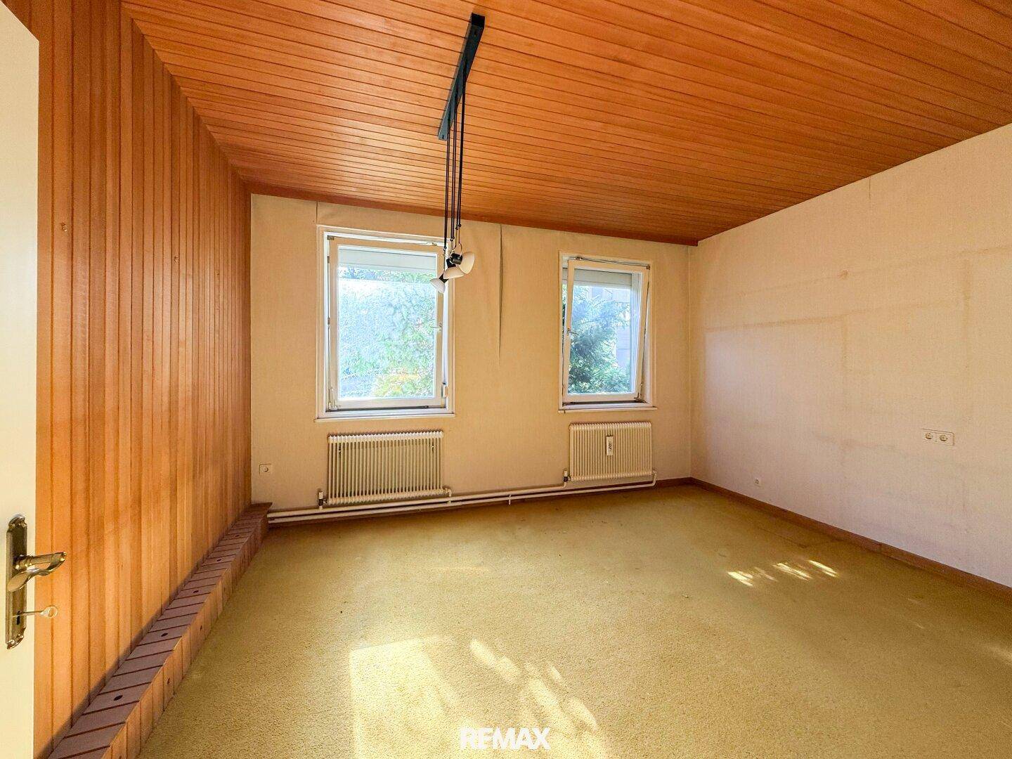 Zimmer mit Teppichboden, Holzdecke und zwei Fenstern, ideal als Schlafzimmer.