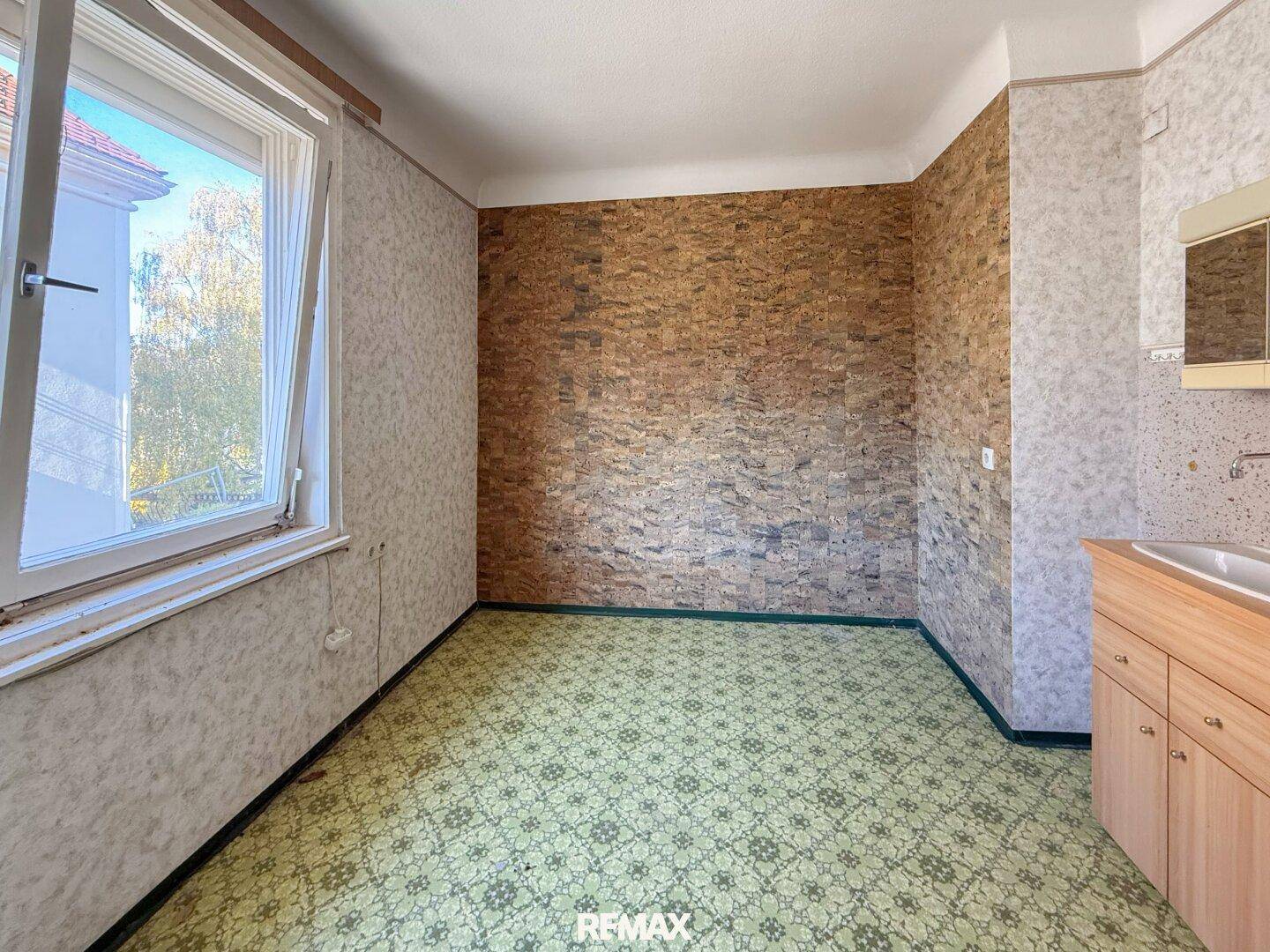 Zimmer mit grünem Linoleumboden, Fenster und einem Waschbecken mit Unterschrank.