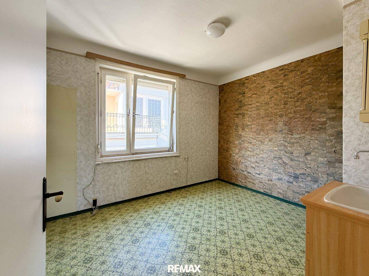 Helles Zimmer mit grünem Linoleumboden, Fenster und einem Waschbecken, das viel Licht bietet.