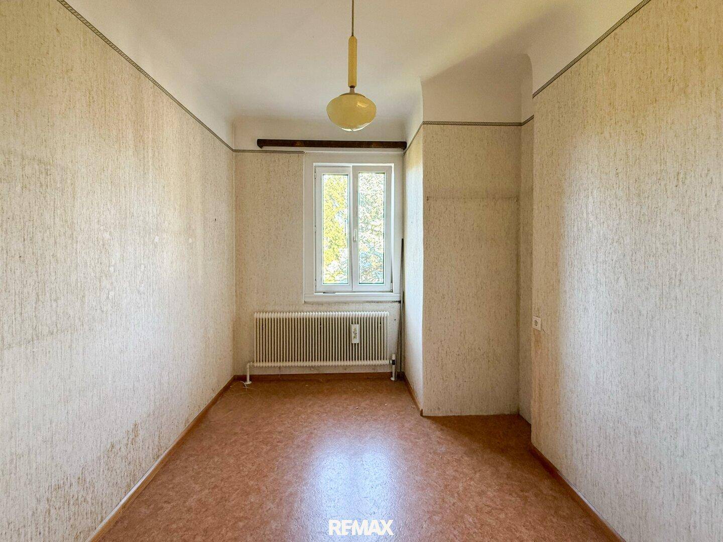 Helles Zimmer mit Korkboden und Heizkörper, bereit für eine Renovierung und individuelle Gestaltung.