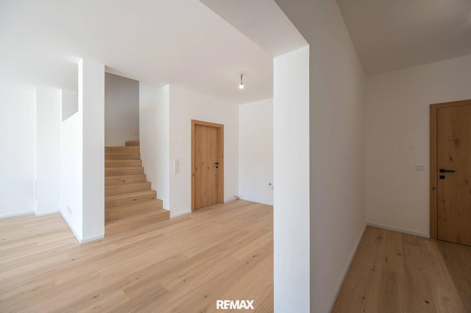 Heller Eingangsbereich mit Holztreppe und Eichenparkettboden, der zu weiteren Räumen führt.