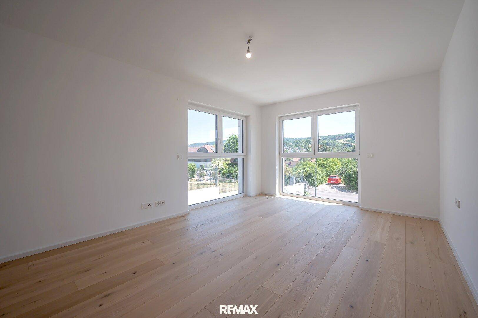 Helles Wohnzimmer mit Eichenparkettboden und großen Fenstern, die viel Tageslicht hereinlassen und Ausblick bieten.