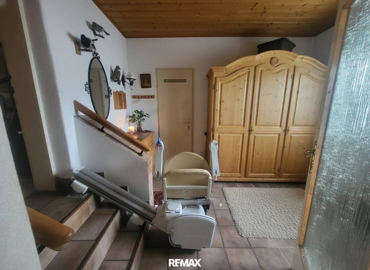 Eingangsbereich mit Holzdecke, gefliestem Boden und einem Treppenlift für Barrierefreiheit.