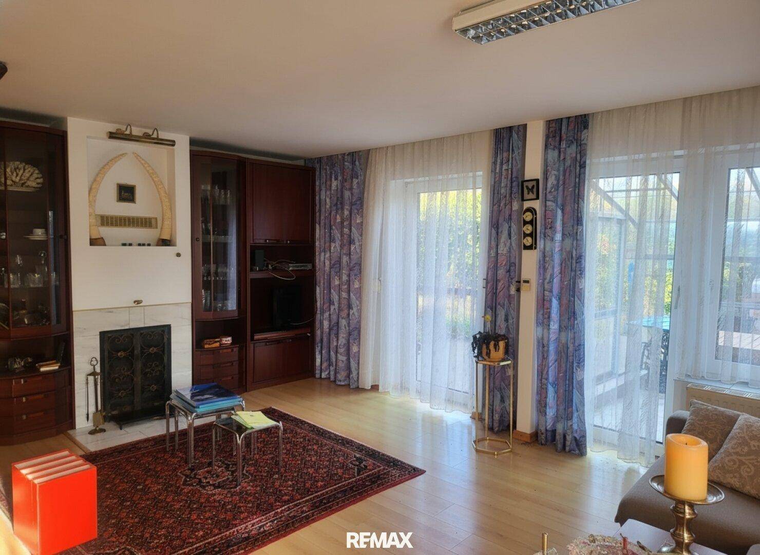 Geräumiges Wohnzimmer mit Kamin, Holzfußboden und großen Fenstern zum Garten.