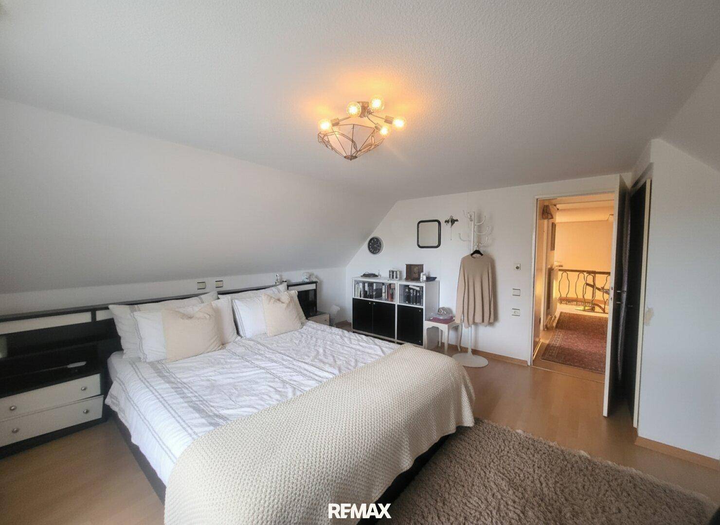 Helles Schlafzimmer im Dachgeschoss mit Doppelbett, Teppich und Zugang zum Flur.