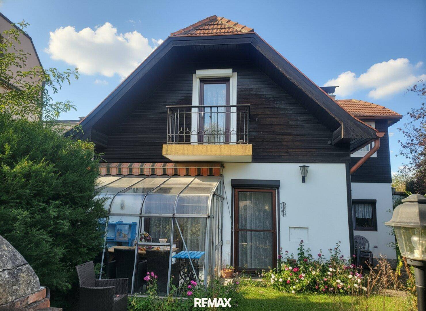 Rückseite des Hauses mit Balkon, Wintergarten und blühenden Blumenbeeten.