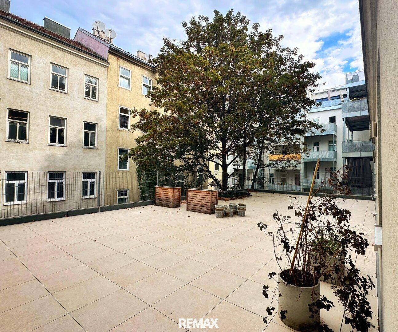 Große, geflieste Außenterrasse mit Bäumen und Blick auf umliegende Gebäude.