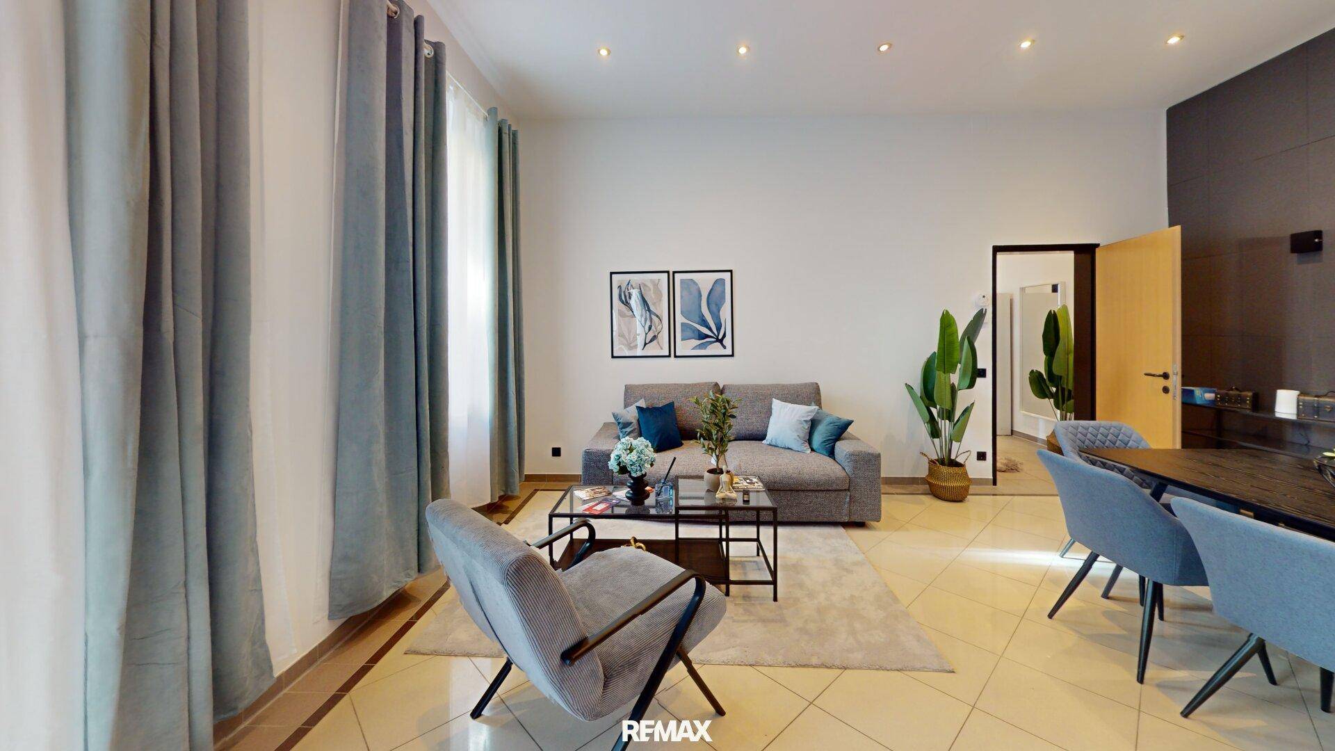 Modernes Wohnzimmer mit Fliesenboden, bequemen Möbeln und indirekter Deckenbeleuchtung.