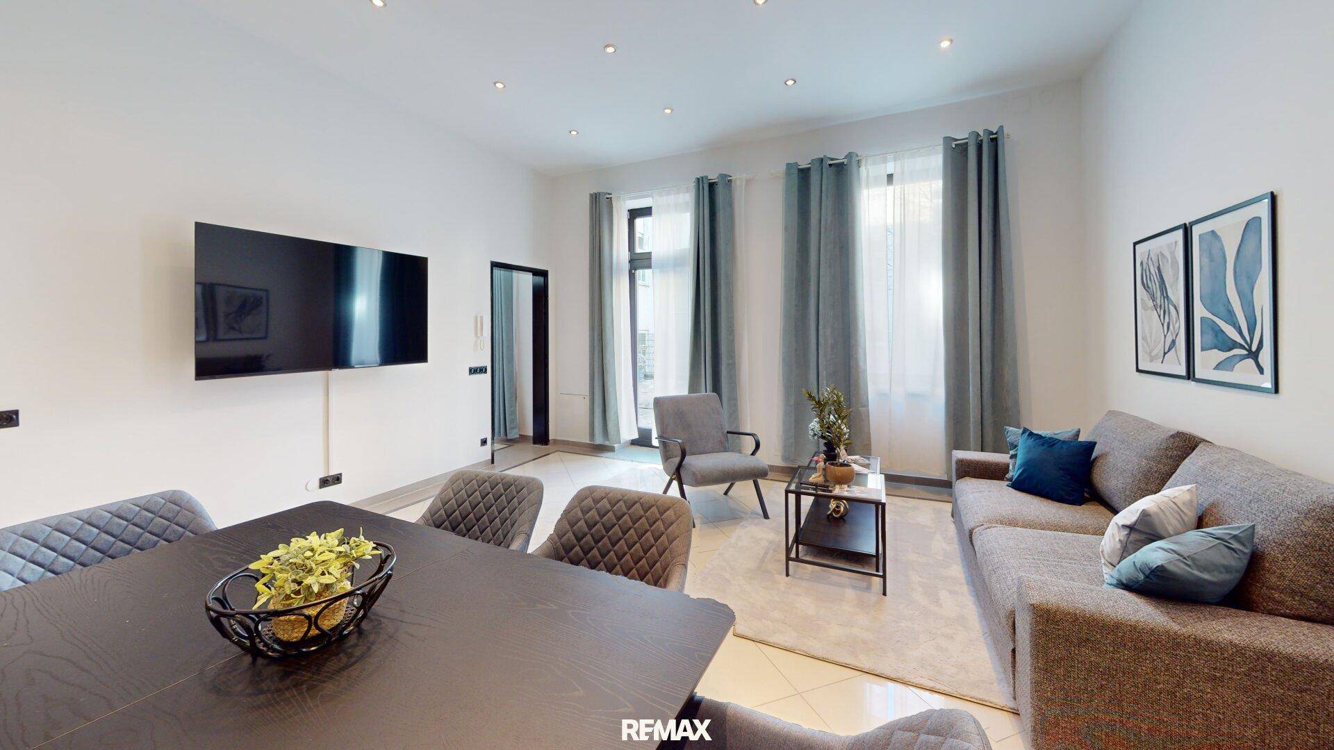Heller Wohn-Essbereich mit großem Fernseher, bequemen Sofas und Zugang zu einem Balkon oder Terrasse.