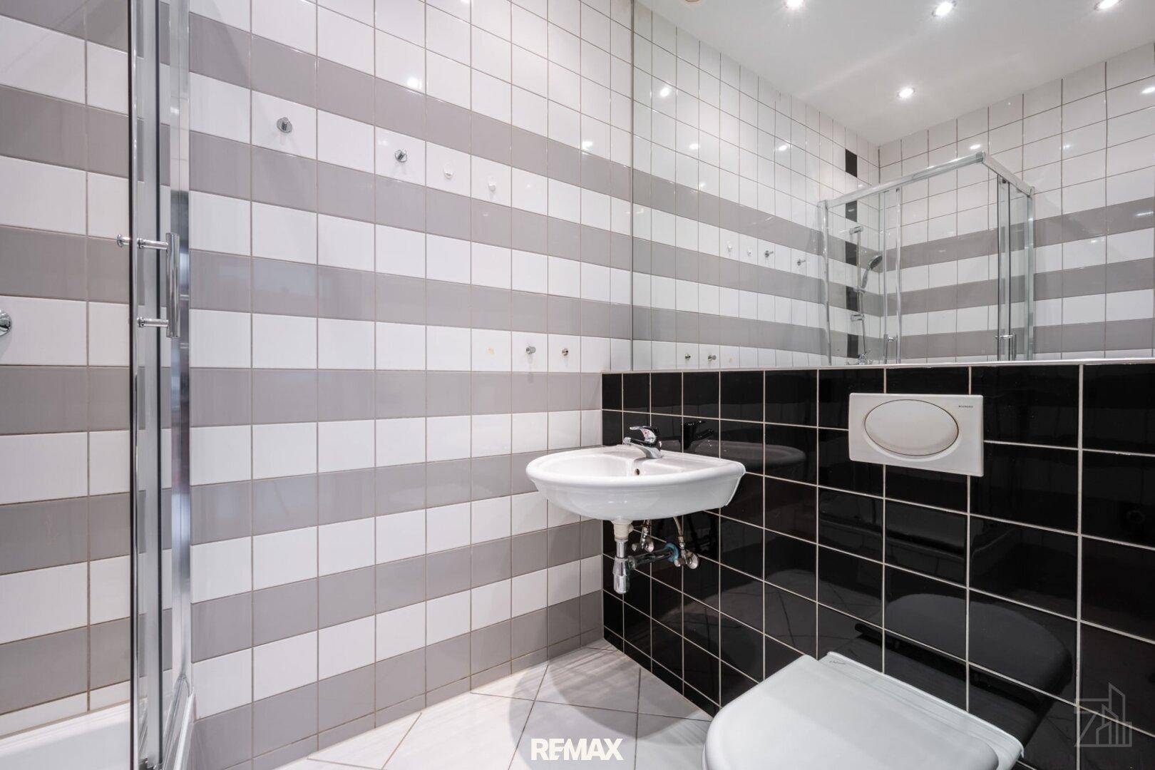 Badezimmer mit markanten schwarz-weiß-grauen Fliesen, einem Waschbecken, Toilette und einer Duschkabine.