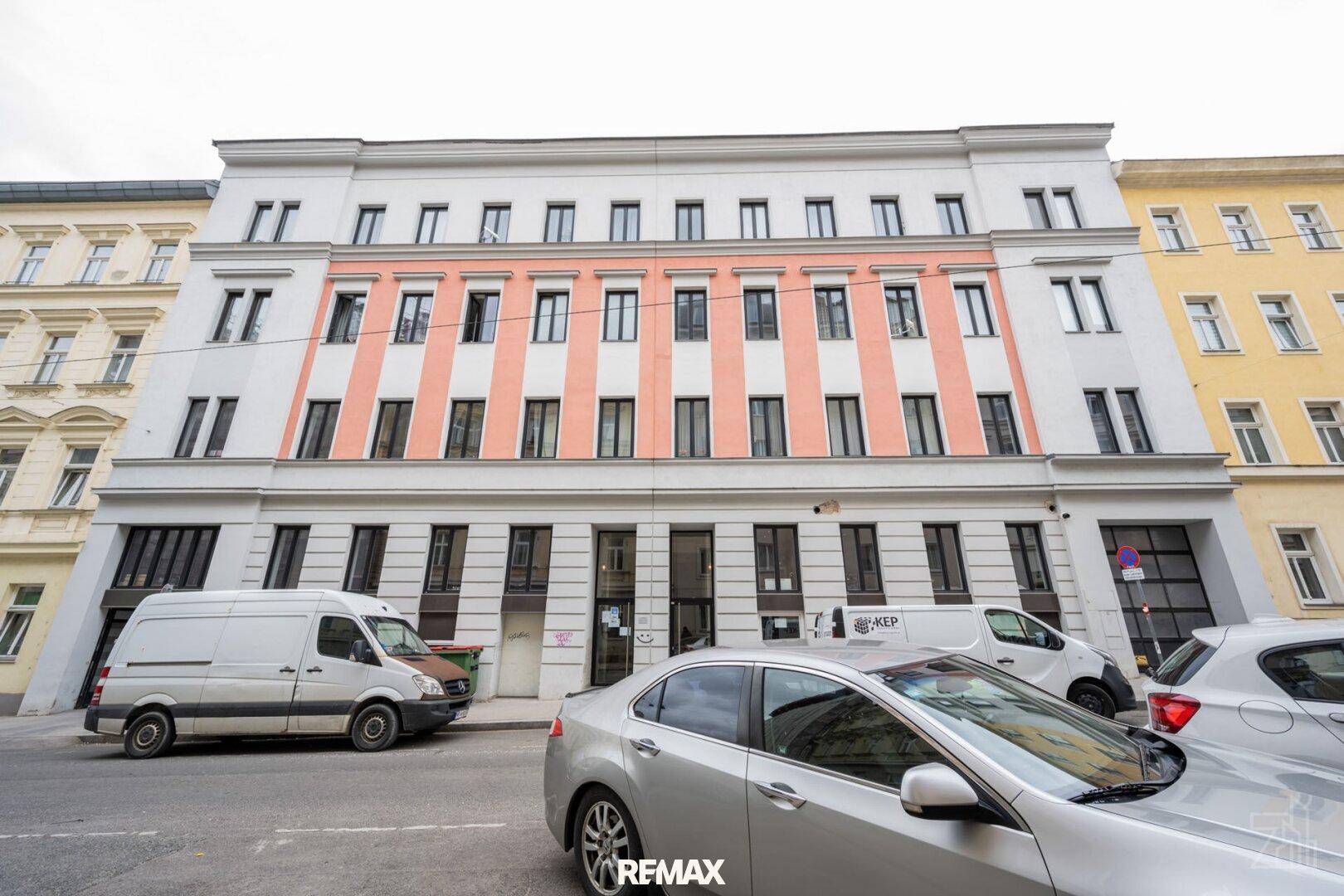 Fassade eines modernen Gebäudes mit markanten rosa und weißen Streifen an einer städtischen Straße.