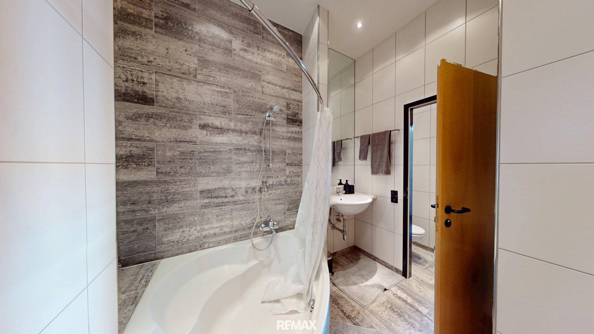 Modernes Badezimmer mit Badewanne, Duschvorhang und stilvollen Fliesen in Holzoptik.
