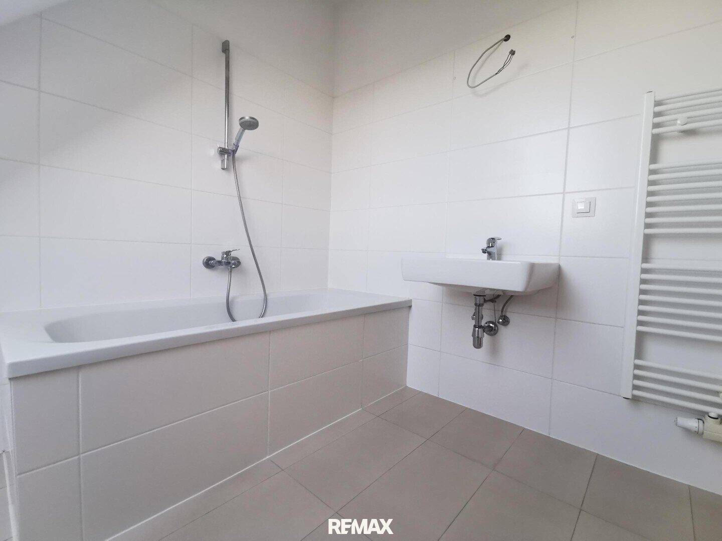 Funktionales Badezimmer mit Badewanne, Duschfunktion, Waschbecken und beheiztem Handtuchhalter.