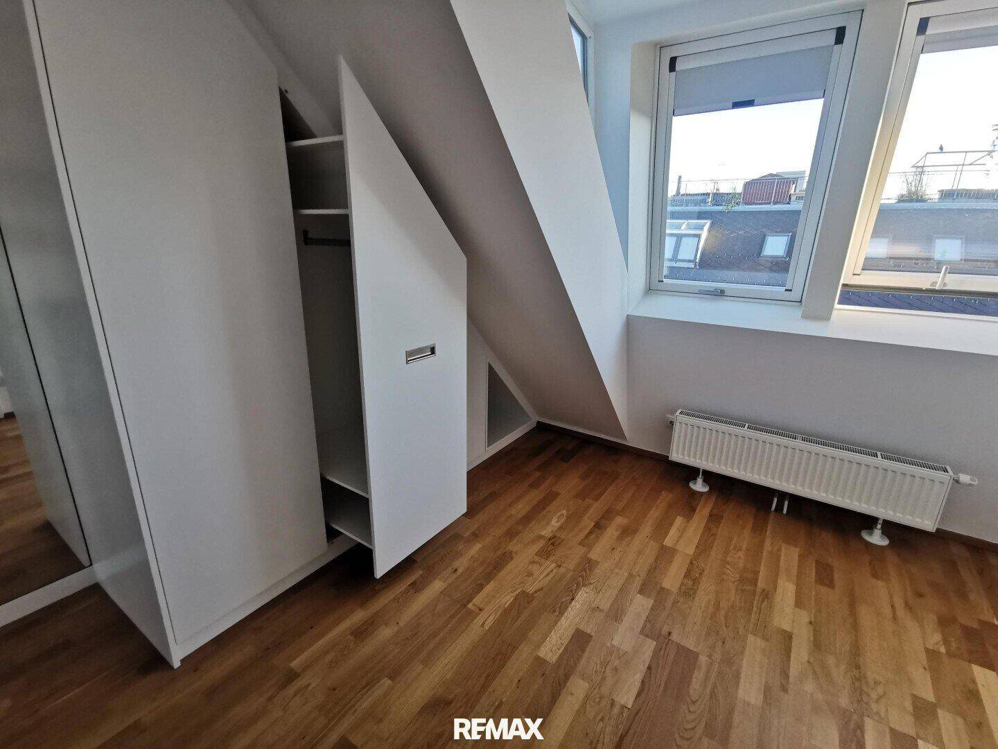 Schlafzimmer mit maßgefertigten Einbauschränken unter der Dachschräge, Parkettboden und Fenster.
